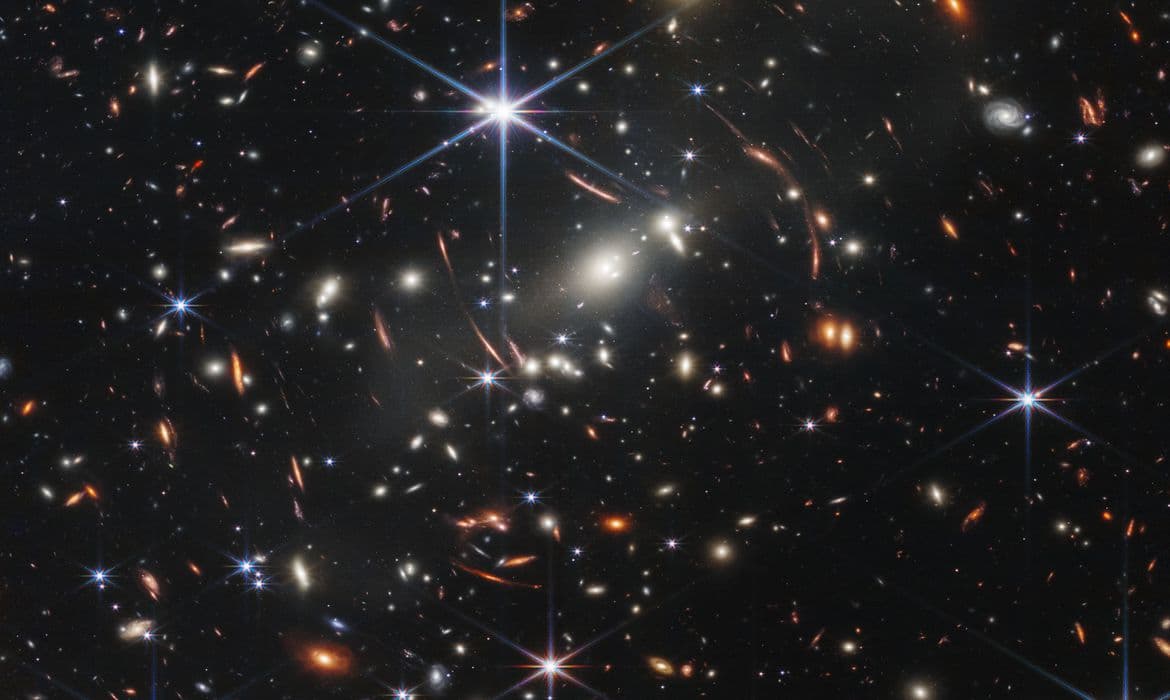 Esta foto mostra lentes gravitacionais e muitas galáxias brilhantes, mas as galáxias menores, mais fracas e menos distintas nesta imagem, são algumas das luzes mais antigas já detectadas por um objeto feito pelo homem. NASA/STScI